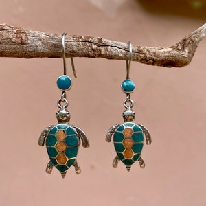 May include: A pair of silver dangle earrings featuring turquoise and orange turtle charms. The turtles have a detailed mosaic design.
