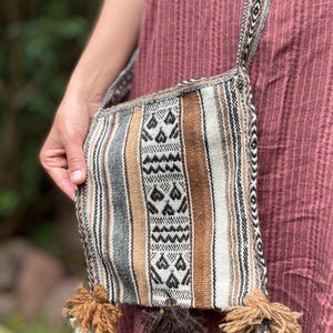 May include: A brown and white striped crossbody bag with black geometric patterns and tassels. The bag is made of woven fabric.