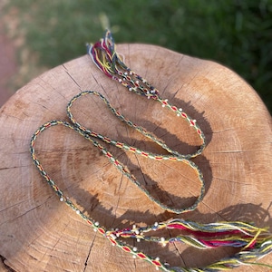 May include: A multi-colored braided cord with white beads, featuring red, green, yellow, and blue threads.