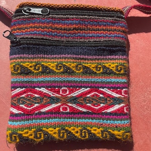 May include: A small, colorful woven bag with a zipper closure. The bag has a strap and is made of a variety of colors, including red, blue, yellow, and green.