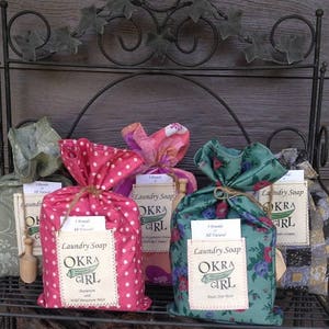 May include: Three bags of laundry soap, each wrapped in a different patterned fabric. The bags are labeled "Laundry Soap Okra Girl" and are all natural.