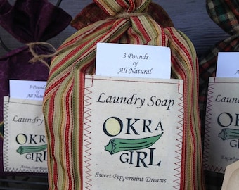 May include: A fabric bag of laundry soap with a striped pattern in red, green, and tan. The label reads "Laundry Soap OKRA GIRL Sweet Peppermint Dreams." A tag reads "3 Pounds of All Natural."