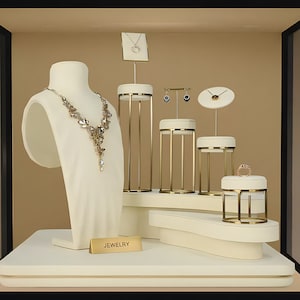 May include: A white jewelry display with gold accents features a necklace, earrings, and a ring. The display is labeled "JEWELRY".