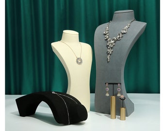 May include: Three jewellery display stands with a grey, white and black velvet finish. The stands are used to display a necklace, earrings and a ring. The necklace is a silver chain with a large, round pendant. The earrings are silver with purple stones. The ring is gold with a clear stone.