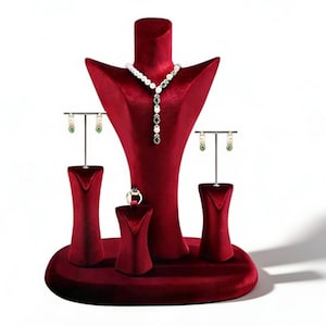May include: A red velvet jewelry display stand showcasing a necklace, earrings, and a ring. The necklace features white and green stones, while the earrings and ring have green accents. The stand is designed to highlight jewelry.