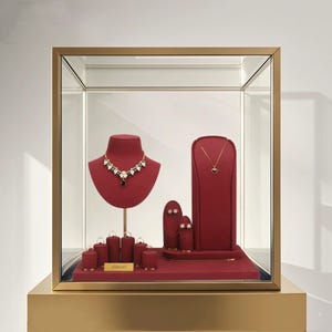 Può includere: Una vetrina dorata che espone gioielli. All'interno, un espositore in velluto rosso contiene una collana con dettagli neri e bianchi, una collana con pendente e vari orecchini e anelli. L'espositore poggia su una base dorata.
