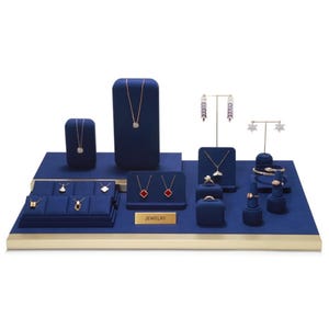 Op de afbeelding: Een sieradendisplay-set van marineblauw fluweel met meerdere standaards, kettingbustes en ringhouders. De set bevat goudkleurige metalen accenten, een gouden plaatje met de tekst JEWELRY en diverse kettingen, oorbellen en ringen op de blauwe oppervlakken.