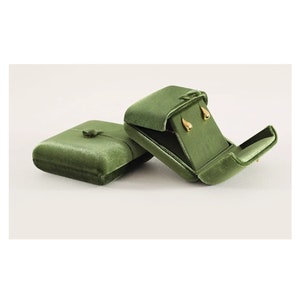 May include: Two olive green velvet jewelry boxes. One box is closed with a small button closure, while the other is open, revealing a pair of small, gold-toned teardrop-shaped stud earrings secured inside the matching green velvet interior lining.