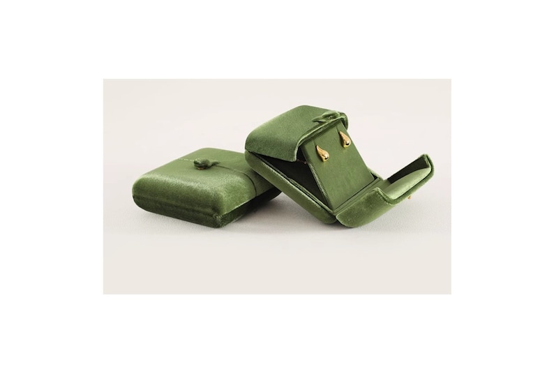 May include: Two olive green velvet jewelry boxes. One box is closed with a small button closure, while the other is open, revealing a pair of small, gold-toned teardrop-shaped stud earrings secured inside the matching green velvet interior lining.