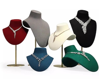 May include: Six jewellery display busts in red, grey, cream, black, blue, and green velvet, each mounted on a gold-toned metal stand. Five of the busts feature silver-toned necklaces with clear crystal accents in various floral and leaf-like designs.