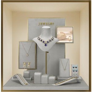 May include: A jewelry display with a variety of necklaces, earrings, and bracelets. The display is made of gray velvet and has a gold frame. The text "JEWELRY" is displayed at the top of the display.