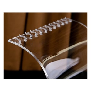 Peut inclure: Un pr&eacute;sentoir transparent en acrylique de forme incurv&eacute;e. Le pr&eacute;sentoir comporte une s&eacute;rie de petits &eacute;l&eacute;ments en forme de crochets le long du bord sup&eacute;rieur. Il est con&ccedil;u pour contenir et pr&eacute;senter des articles, en mettant l'accent sur la clart&eacute; et la visibilit&eacute;.