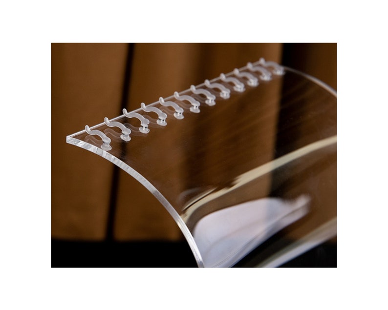 Peut inclure: Un pr&eacute;sentoir transparent en acrylique de forme incurv&eacute;e. Le pr&eacute;sentoir comporte une s&eacute;rie de petits &eacute;l&eacute;ments en forme de crochets le long du bord sup&eacute;rieur. Il est con&ccedil;u pour contenir et pr&eacute;senter des articles, en mettant l'accent sur la clart&eacute; et la visibilit&eacute;.