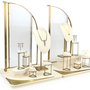 Może przedstawiać: Złoty stojak na biżuterię z białą podstawą i przezroczystymi panelami akrylowymi. Stojak ma wiele poziomów do prezentacji naszyjników, kolczyków, pierścionków i bransoletek. Stojak jest oznaczony jako "Jewelry Way".