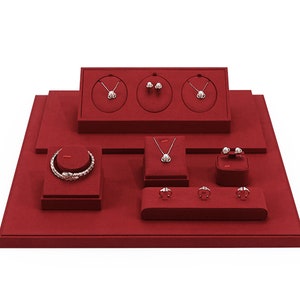 Può includere: Un espositore per gioielli in velluto rosso con più scomparti per esporre collane, braccialetti, orecchini e anelli. L'espositore è realizzato in un materiale morbido e vellutato e ha un design moderno e minimalista.
