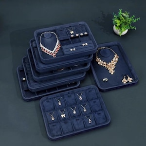 May include: A selection of navy blue velvet jewellery display trays. The trays hold necklaces, earrings, and rings. Some trays have necklace busts. The jewellery includes a variety of styles, including a red and white necklace and gold necklaces.