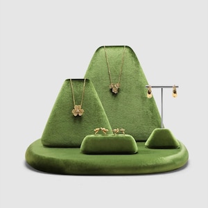 Könnte beinhalten: Ein Schmuckständer-Set aus grünem Samt mit zwei gestuften dreieckigen Ständern, einer kleinen rechteckigen Leiste und einem T-förmigen Ohrringhalter. Das Set präsentiert zwei goldene Halsketten mit Blumenanhängern, zwei Ringe und zwei Ohrringe.
