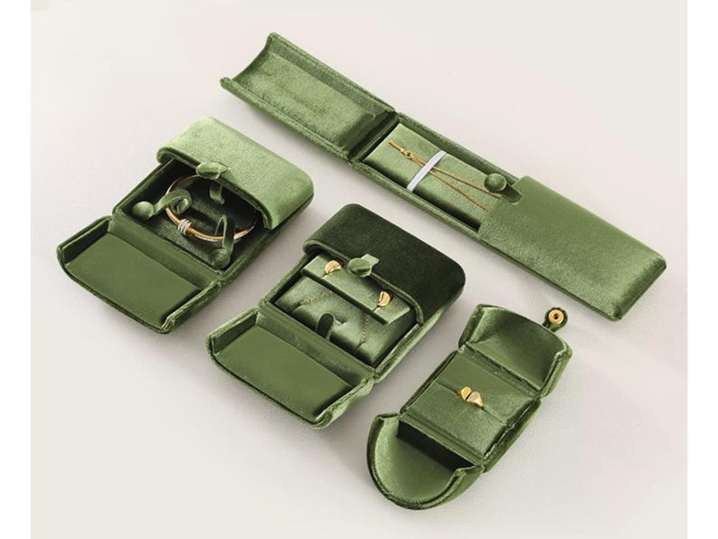 May include: A collection of four olive green velvet jewelry boxes in various shapes and sizes. The set includes a long rectangular case, a square box, a small ring box, and a larger square box, all featuring soft velvet linings and snap closures.