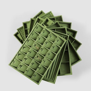 May include: A collection of olive green jewelry display trays. Each tray has multiple compartments for rings, earrings, and other small jewelry items. The trays are arranged in a fan-like pattern, showcasing the storage capacity.