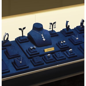 May include: A display case filled with various jewelry pieces. The jewelry includes necklaces, earrings, rings, and bracelets, all presented on blue velvet stands. A gold sign reads "JEWELRY".
