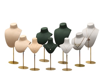 May include: Set of eight jewellery display busts with gold stands. The busts are made of fabric and come in beige, green and grey.