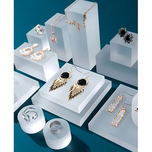 以下が含まれることがあります： 様々な形のイヤリング、リング、ネックレスなどのジュエリーを飾った、透明なアクリル製のディスプレイスタンドの詰め合わせ。スタンドは様々な形とサイズがあり、ジュエリーは視覚的に魅力的な方法で配置されています。