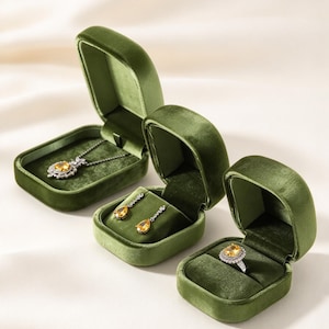 May include: Three olive green velvet jewelry boxes containing a silver necklace with a yellow pear-shaped pendant, a pair of silver drop earrings with yellow pear-shaped stones, and a silver ring featuring a yellow oval-shaped center stone.
