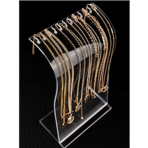 Peut inclure: Un pr&eacute;sentoir &agrave; bijoux en acrylique transparent pr&eacute;sentant plusieurs colliers dor&eacute;s. Les colliers varient en style, y compris des mod&egrave;les &agrave; cha&icirc;ne et &agrave; perles. Le pr&eacute;sentoir a un design incurv&eacute; et une base robuste.