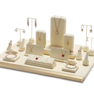 May include: A white jewelry display stand with multiple compartments for rings, earrings, necklaces, and bracelets. The stand is made of a soft, padded material and has a gold trim.