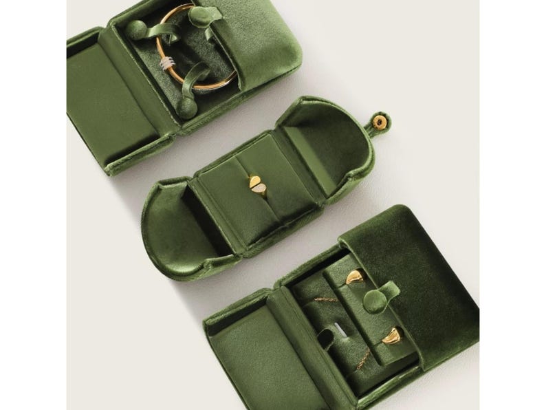 May include: Three olive green velvet jewelry boxes with gold-tone snap closures. The top box holds a gold bangle, the middle box contains a gold heart-shaped ring, and the bottom box displays a gold chain necklace with two small gold stud earrings.