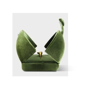 May include: An olive green velvet ring box with a hinged lid that opens upward to reveal a gold ring centered inside. The exterior of the box features a soft, textured fabric finish, while the interior is lined with matching green material.