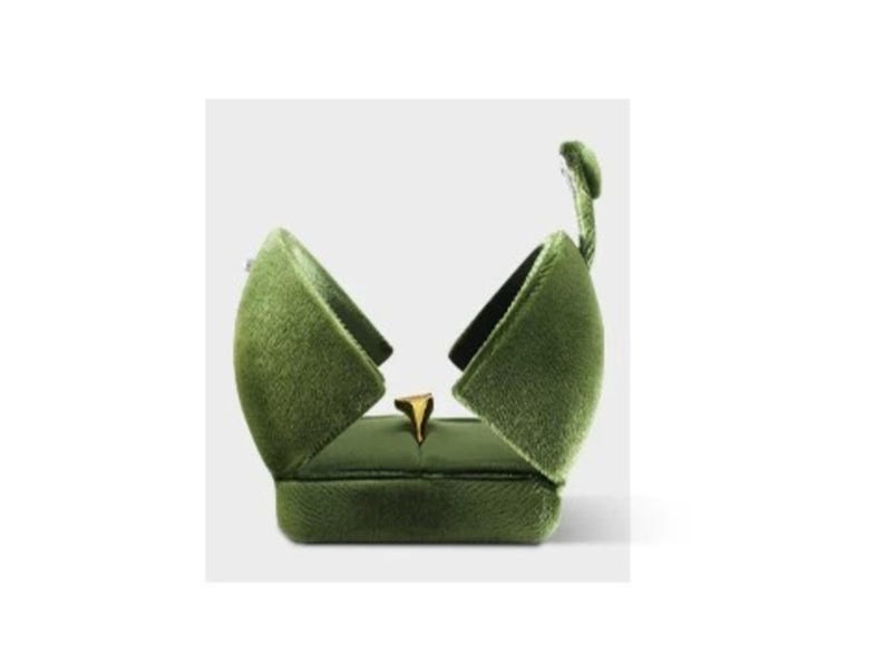 May include: An olive green velvet ring box with a hinged lid that opens upward to reveal a gold ring centered inside. The exterior of the box features a soft, textured fabric finish, while the interior is lined with matching green material.