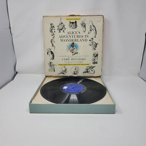 May include: Vintage vinyl record of "Alice's Adventures in Wonderland" by Cyril Ritchard. The album cover features illustrations of characters from the story. The record is in a box with a light blue interior.