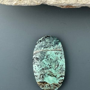 May include: A green and black oval cabochon gemstone with a swirling pattern.