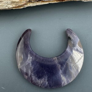 May include: A crescent moon shaped piece of polished amethyst with a purple and white marbled pattern.
