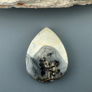 May include: A teardrop-shaped pendant made of white and black agate with a swirling pattern. The pendant is polished and has a smooth surface.