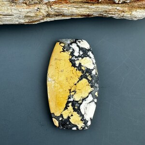 Puede incluir: Una piedra preciosa cabuj&oacute;n ovalada de color amarillo, negro y blanco con un patr&oacute;n de m&aacute;rmol.