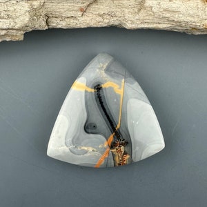 May include: A triangular shaped, polished stone with a gray, white, black, and orange pattern.