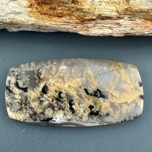 May include: A polished, rectangular slab of agate with a swirling pattern of black, white, and gold. The agate has a smooth, polished surface.