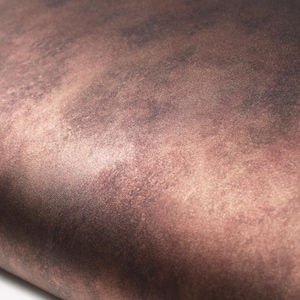 May include: Close-up of a textured surface with a gradient of brown and reddish-brown hues. The surface appears to have a metallic or aged appearance, with subtle variations in colour and texture.
