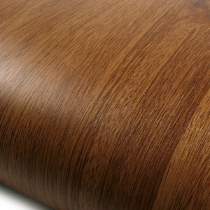 May include: Close-up of a roll of brown wood-look vinyl. The surface has a natural wood grain pattern with varying shades of brown and a slight sheen. The material appears to be flexible and suitable for various DIY projects.