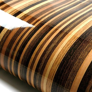 May include: Close-up of a wood laminate sheet with a striped pattern in shades of brown, black, and beige. The laminate has a glossy finish.