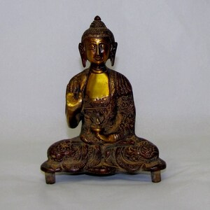 May include: A gold-colored metal statue of a seated Buddha with intricate details on the robe and base. The Buddha has a serene expression and is in a meditative pose.