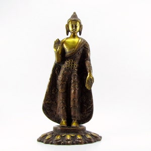 May include: A gold-coloured metal statue of Buddha standing on a decorative base. The statue is wearing a robe with intricate details and has a serene expression.