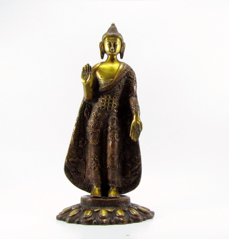 May include: A gold-coloured metal statue of Buddha standing on a decorative base. The statue is wearing a robe with intricate details and has a serene expression.