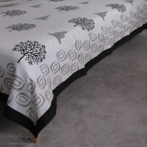 May include: A white bedspread with a black and gray geometric pattern and a black border. The bedspread features a repeating pattern of stylized trees.