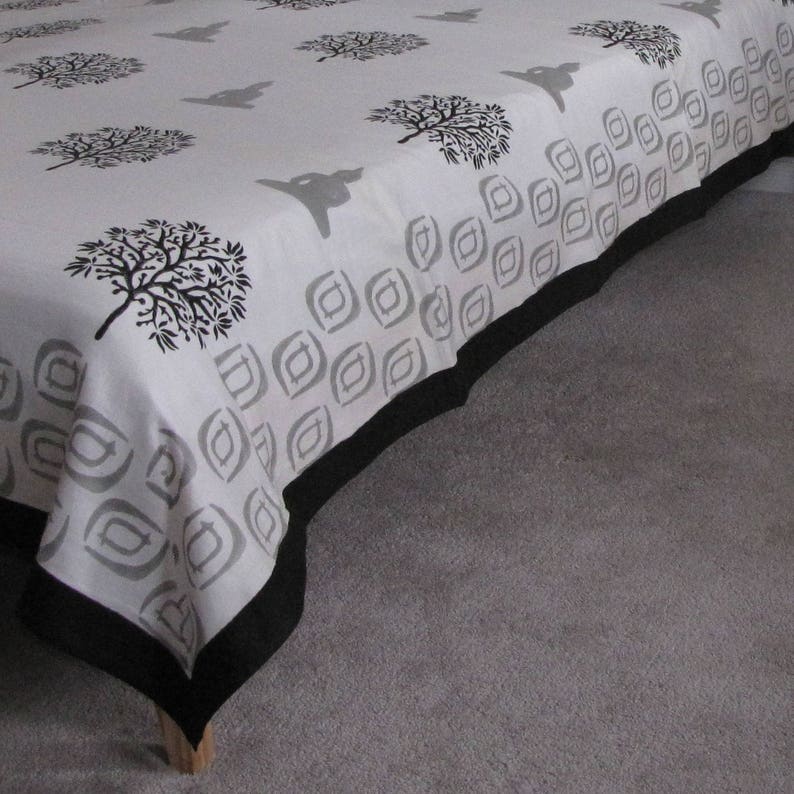 May include: A white bedspread with a black and gray geometric pattern and a black border. The bedspread features a repeating pattern of stylized trees.