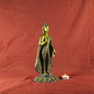 May include: A gold-coloured metal statue of Buddha standing on a decorative base. The statue is wearing a robe with intricate details and has a serene expression.