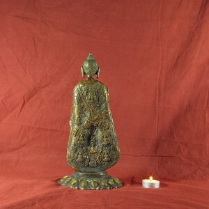 May include: A gold-coloured metal statue of Buddha, standing on a circular base. The statue is intricately detailed with carvings and designs.