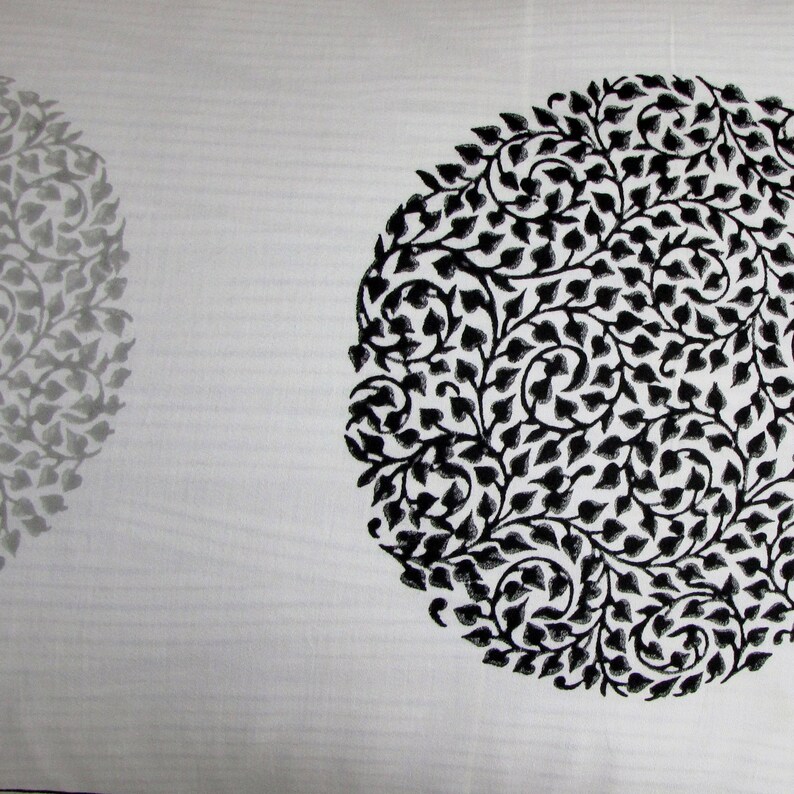 May include: White fabric with a black and gray floral pattern. The pattern is in the shape of a circle.